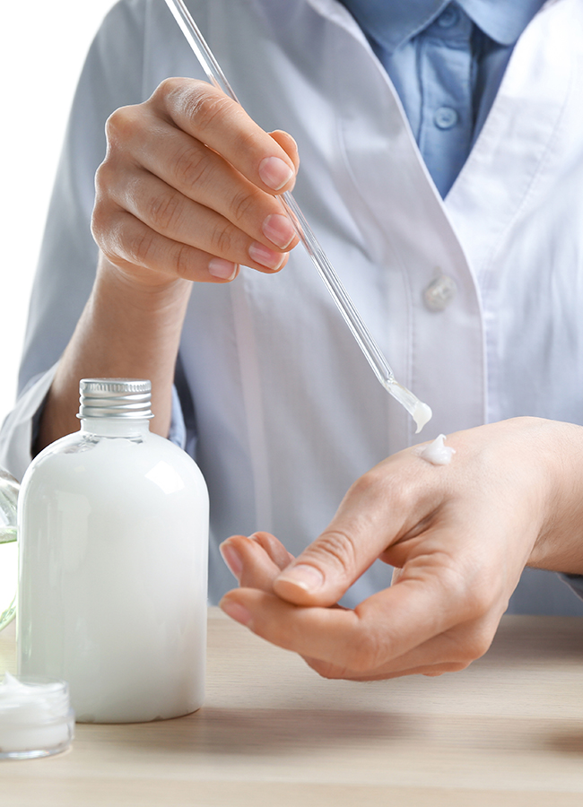 Woman applying natural cream onto hand in cosmetic laboratory, c